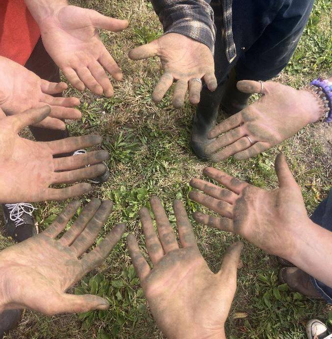 Volunteers holding their hands in a circle with tomato stains on them.